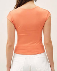 Woman wearing an orange top and white shorts on a plain background