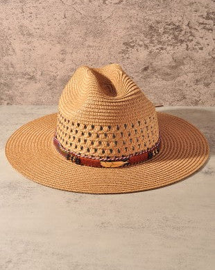 A straw cowboy hat with a wide brim and a decorative band, displayed on a light stone surface against a textured beige wall.