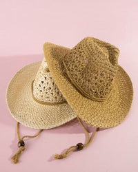 Two straw hats with tassels on a pink background