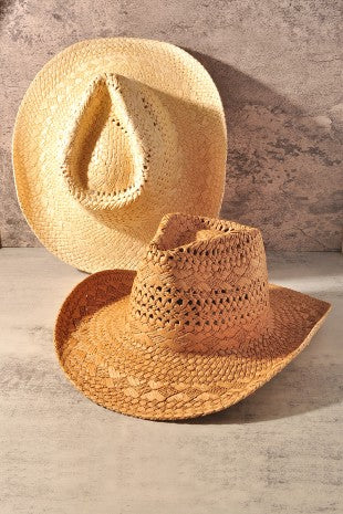 Two woven straw cowboy hats in natural tan tones, one standing upright in the back and one lying flat in the front, set against a textured concrete wall and floor.