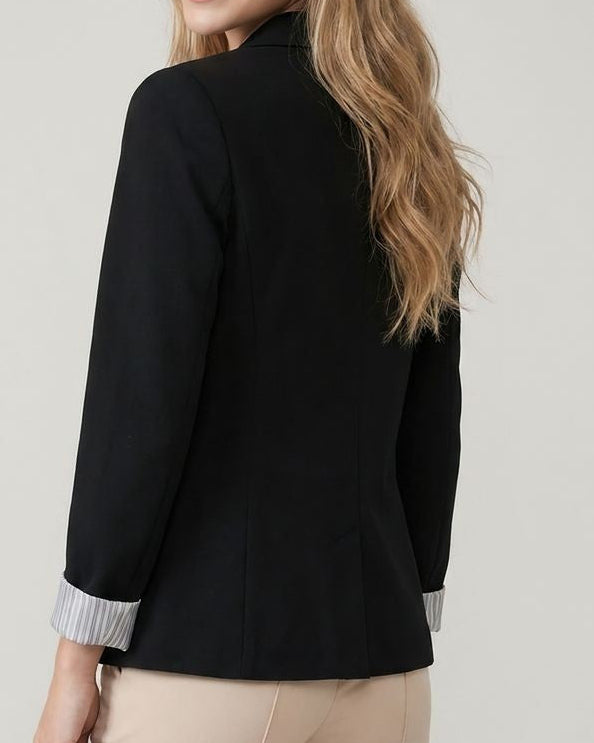 Woman wearing a black blazer and beige pants on a plain background