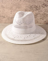 A white crocheted sun hat with a wide brim and a structured crown, displayed against a textured beige background.