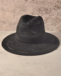 A black woven fedora hat with an intricate openwork pattern, displayed against a textured beige and gray background.