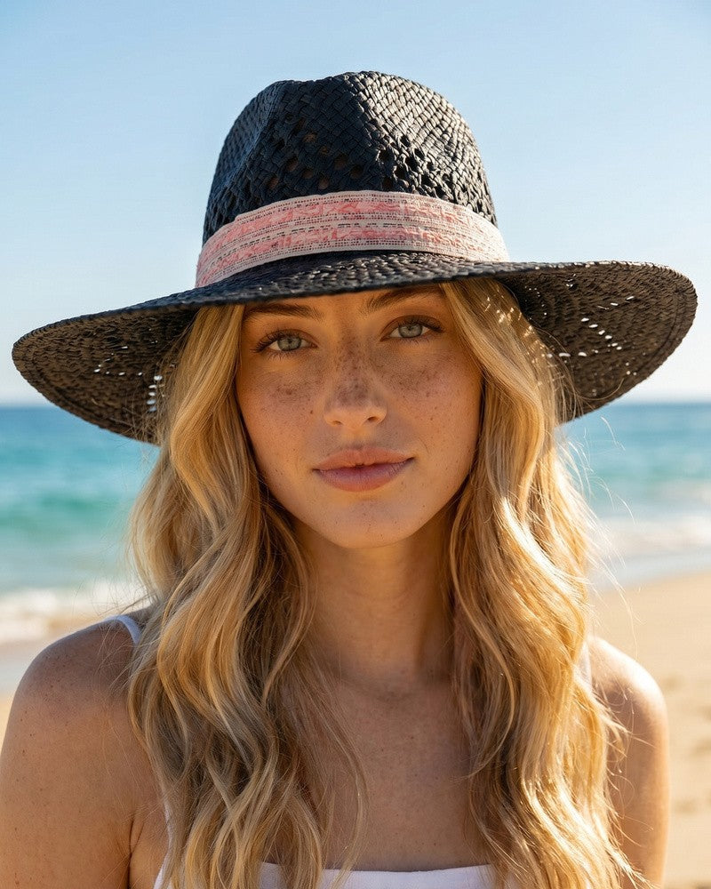 Woman wearing a black straw hat with a pink band on a beach
