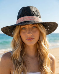 Woman wearing a black straw hat with a pink band on a beach