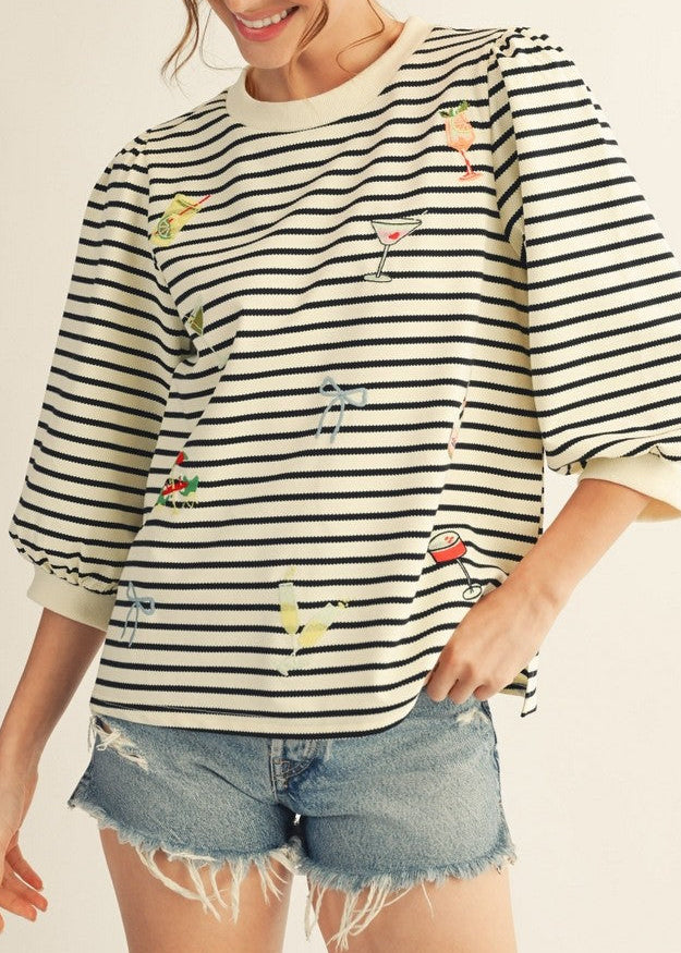Woman wearing a striped shirt with embroidered designs on a plain background